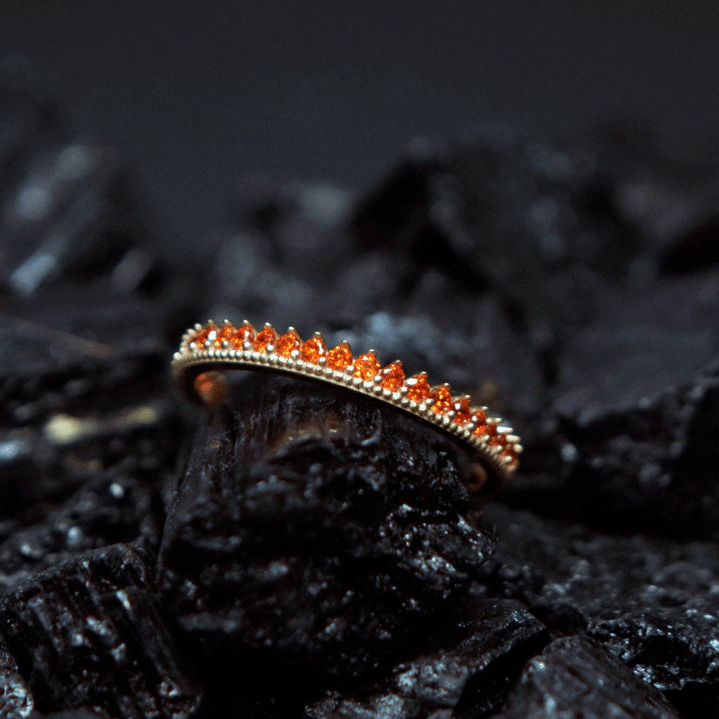 Churumbela con zirconia; en oro color amarillo y zirconias de color naranja con vista al frente sobre piedra obsidiana 