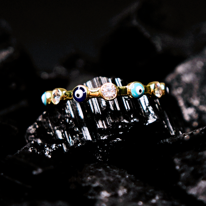 Churumbela con zirconia; en oro color amarillo con zirconias y ojos turcos de colores con vista al frente sobre piedra de obsidiana