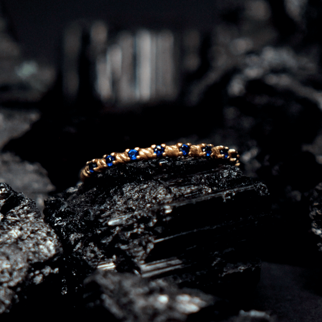 Churumbela con zirconia; en oro color amarillo con zirconias color azul con vista al frente sobre piedra de obsidiana