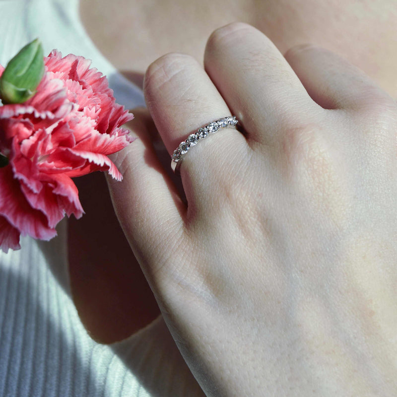 Churumbela con diamante; en oro color blanco en mano vista al frente más cerca junto a flor rosada